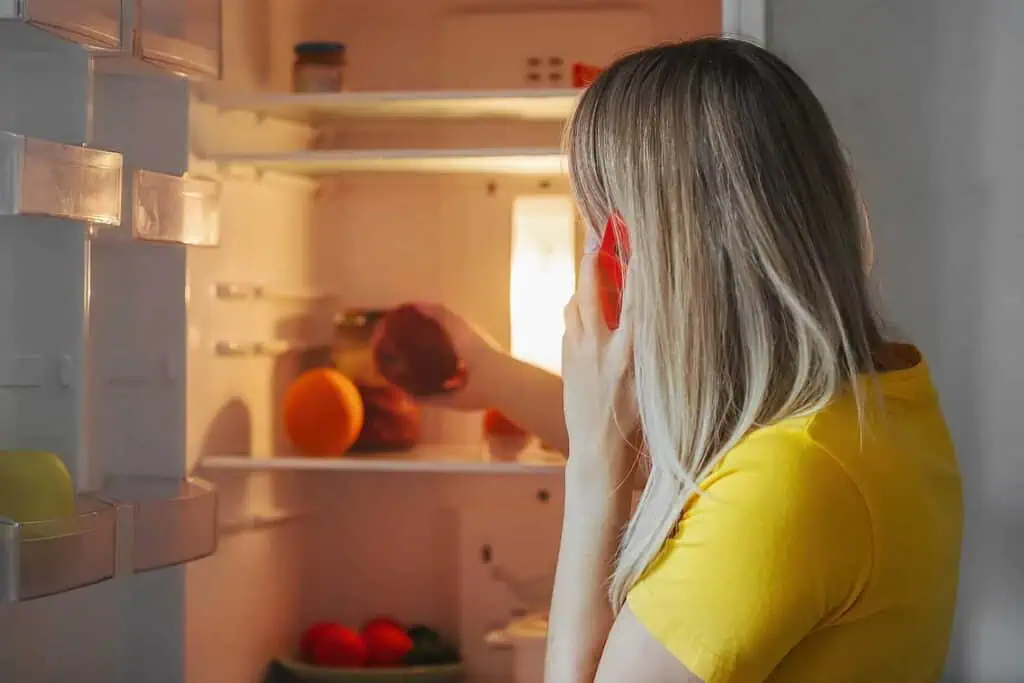 a woman on the phone takes fruit out of her fridge
