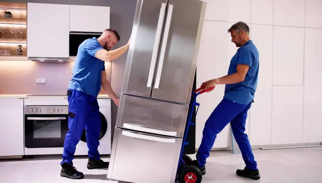 Two movers lift a fridge that has been loaded onto a hand truck/dolly