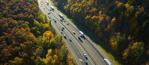 an array of cars and trucks are driving in both directions down a long highway in the middle of a very wooded area