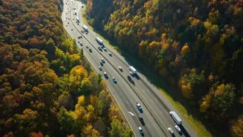 an array of cars and trucks are driving in both directions down a long highway in the middle of a very wooded area