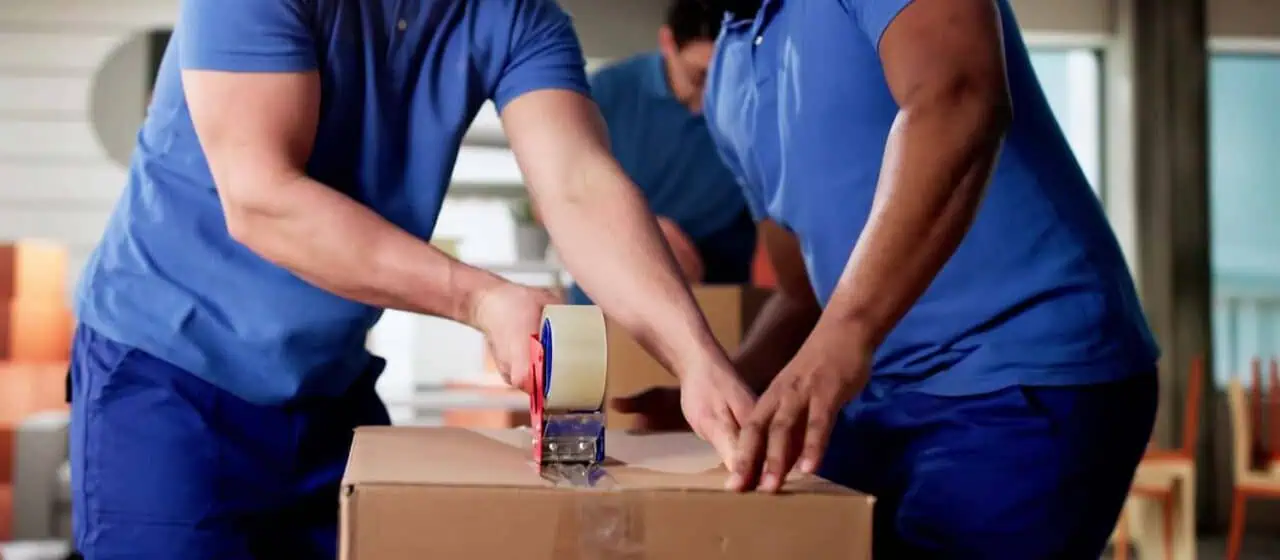 a team of movers in blue uniforms tapes a box shut