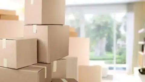 Stacked cardboard moving boxes in a bright living room, ready for a home relocation.