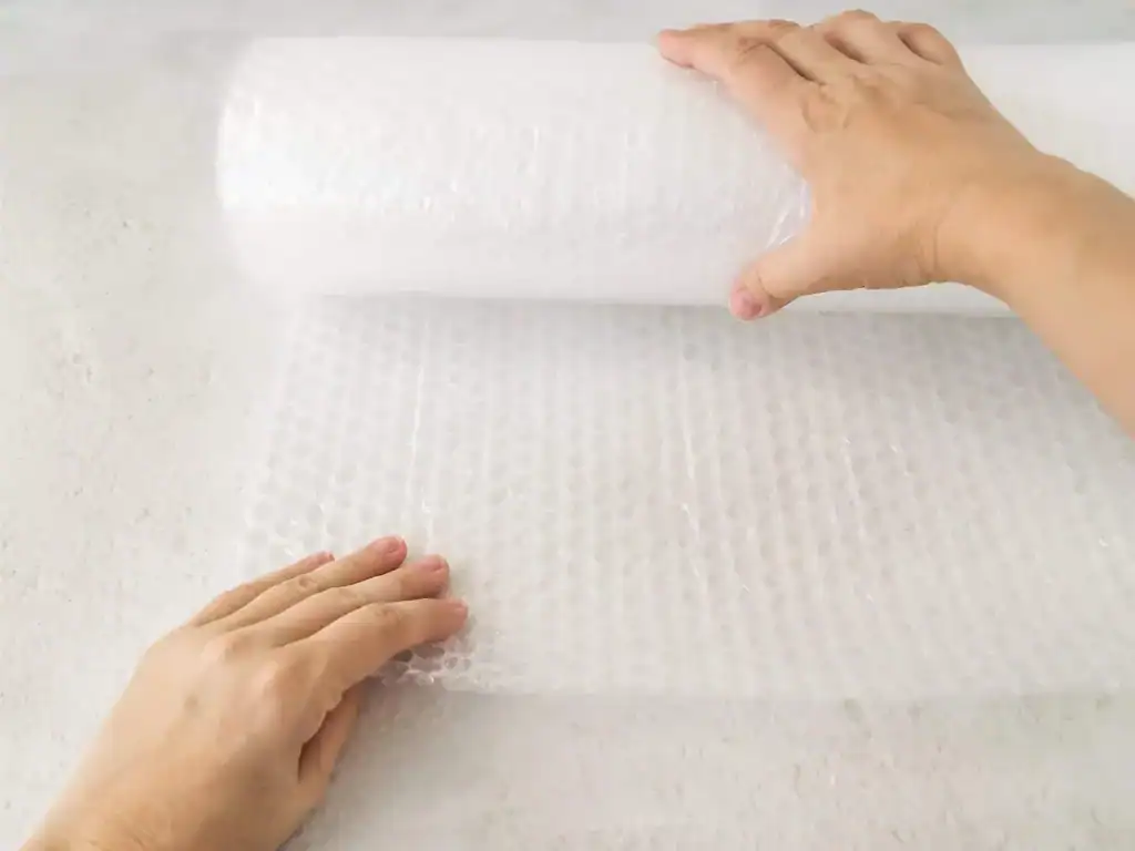Hands rolling out bubble wrap for packing fragile items.