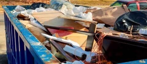 A dumpster full of broken furniture and various other kinds of junk