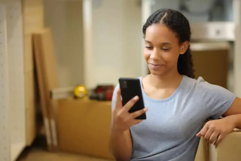 Woman checking best moving apps on phone while preparing for a move with boxes around her