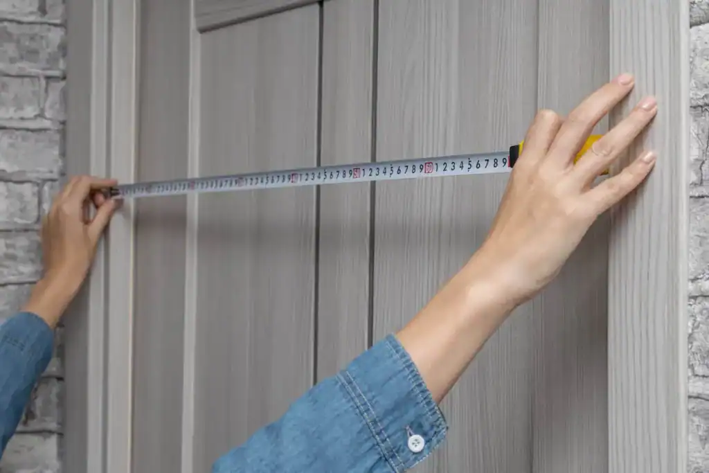 Person measuring doorway width with tape measure before moving furniture.