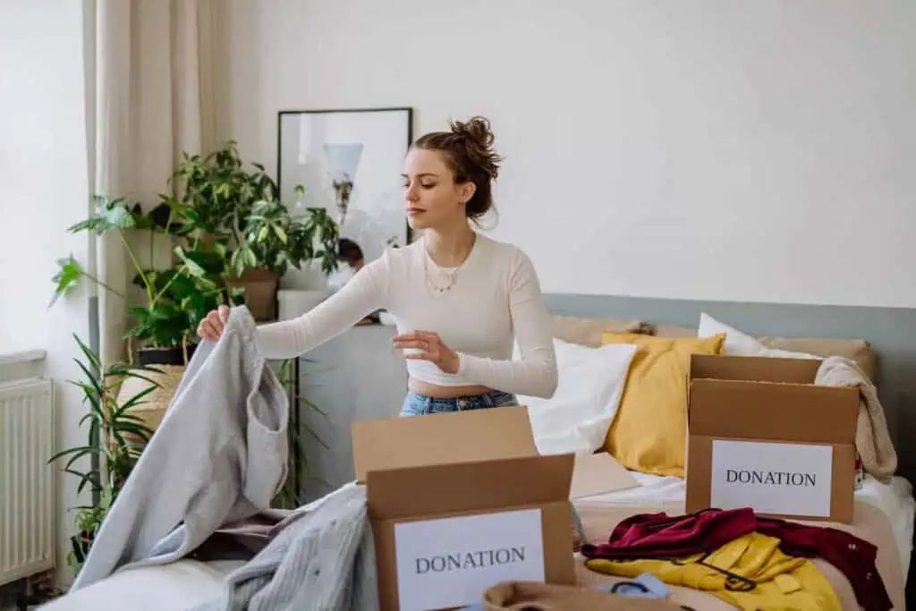 a young woman is organizing her clothing to be donated. There are boxes labeled "donation" around her