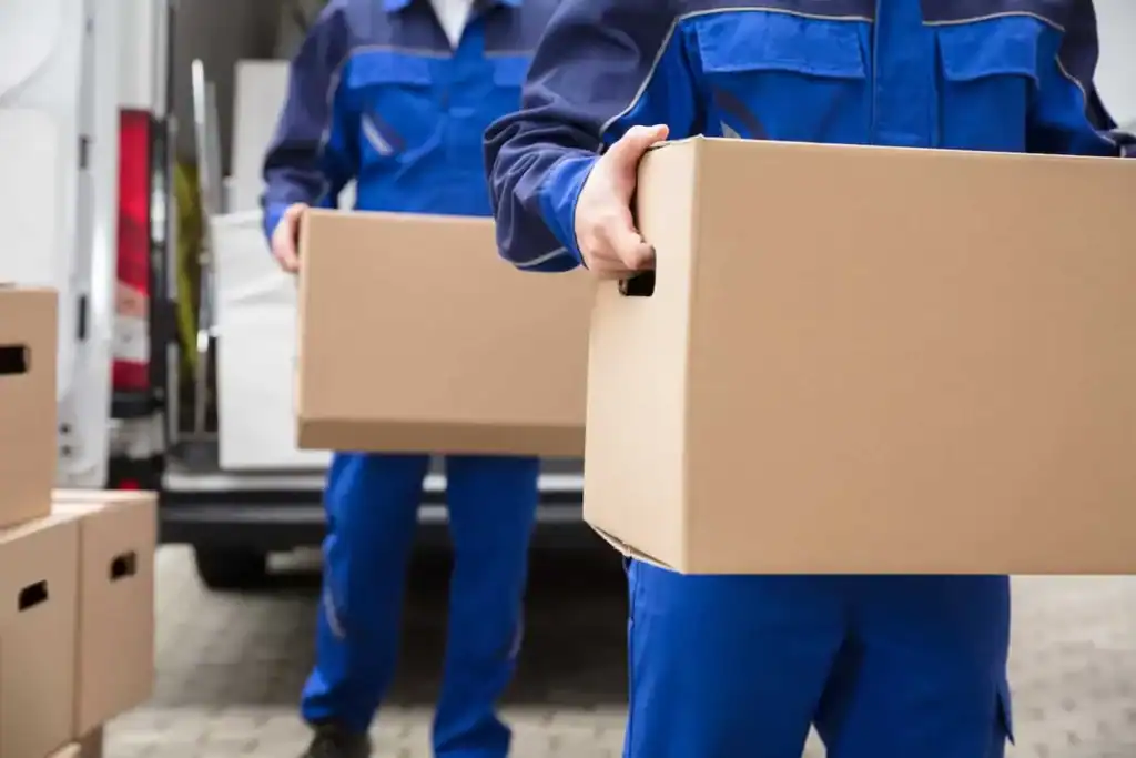 Movers in uniform carrying cardboard moving boxes from a truck