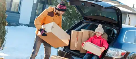 Family unloading moving boxes from a car during a winter move