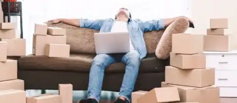 Man overwhelmed by moving stress, surrounded by cardboard boxes and laptop on couch