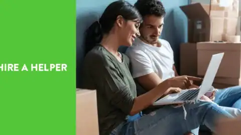 Couple sitting among moving boxes using a laptop to book movers on HireAHelper