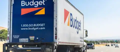 Budget moving truck traveling on open road under clear sky
