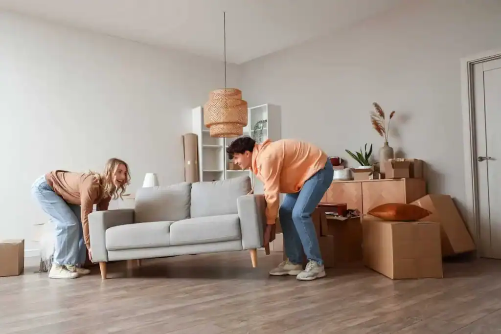 Couple lifting a gray sofa among moving boxes in a living room