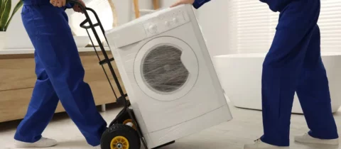 Movers using a dolly to safely transport a washing machine wrapped for moving