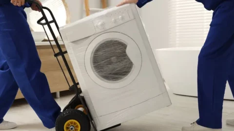 Movers using a dolly to safely transport a washing machine wrapped for moving