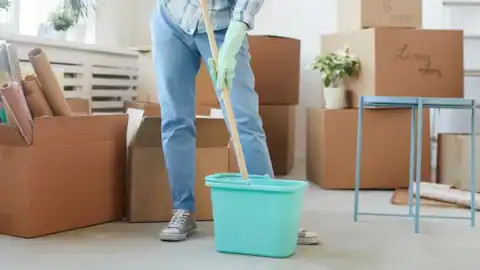 Person mopping the floor in a room filled with moving boxes during a move-out cleaning.