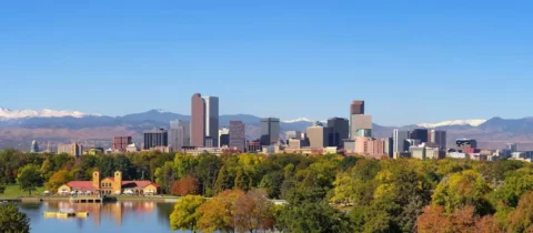 Denver skyline viewed from City Park with fall foliage and mountains in the background.