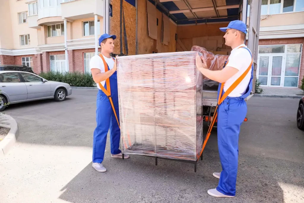 two movers use moving straps to help move a heavy piece of furniture