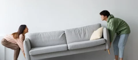 two people work together to lift a gray couch
